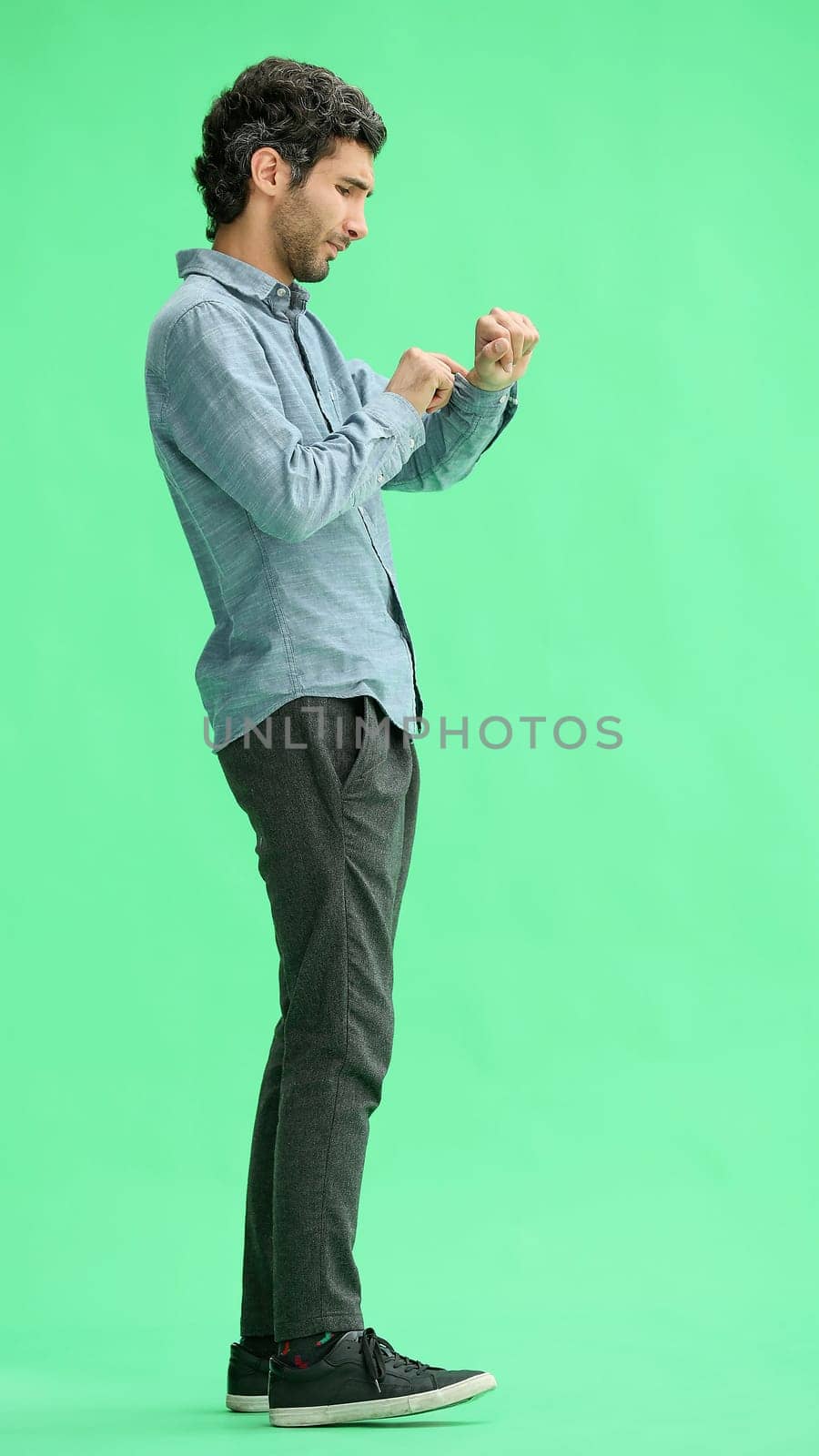 young man in full growth. isolated on green background looking at wristwatch.