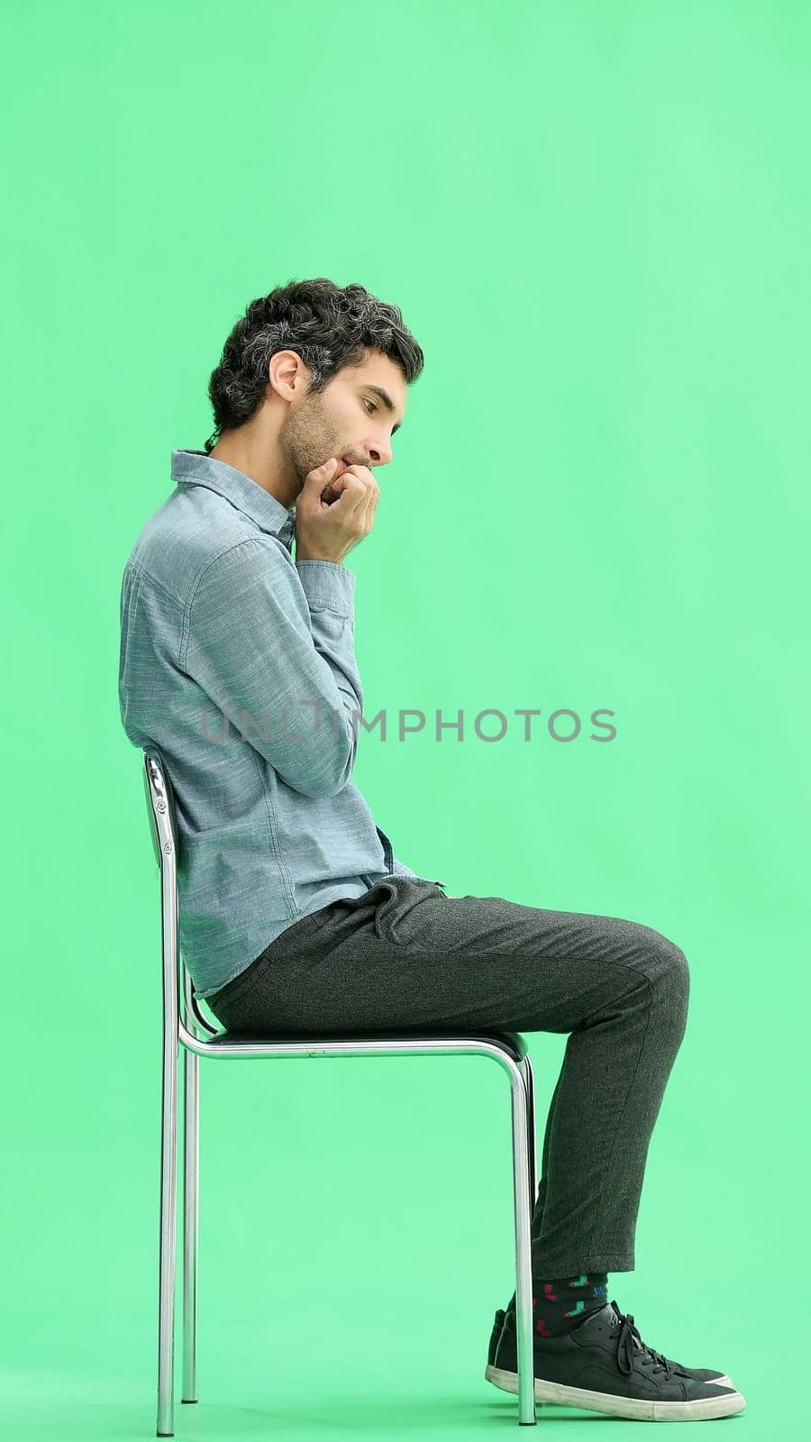 young man in full growth. isolated on a green background sitting on a chair by Prosto