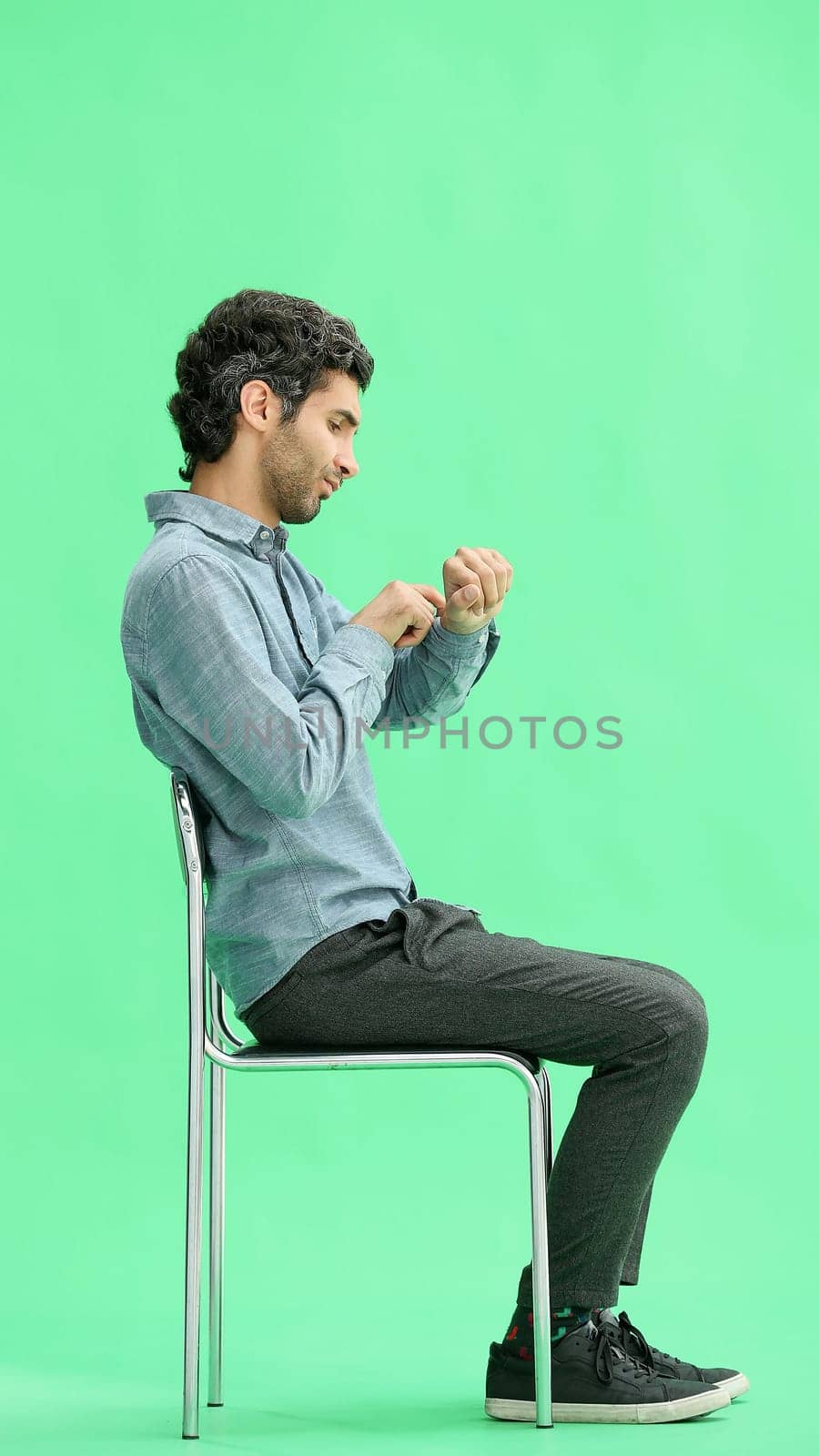 young man in full growth. isolated on a green background sitting on a chair by Prosto