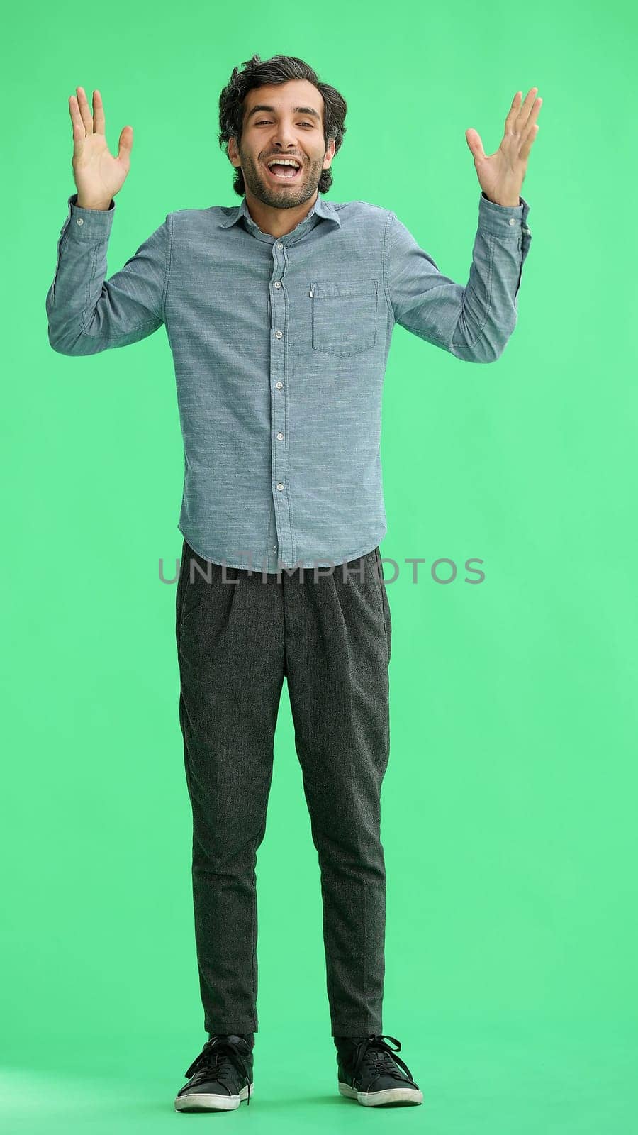 man in full growth. isolated on a green background shows with his hands a sign of what to expect.