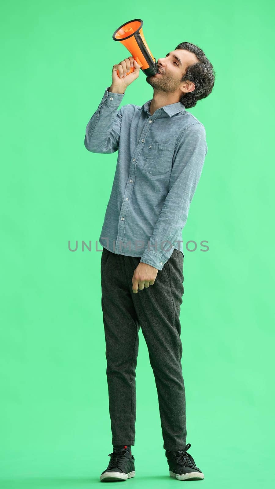 man isolated on a green background in business clothes with a loudspeaker in his hand by Prosto