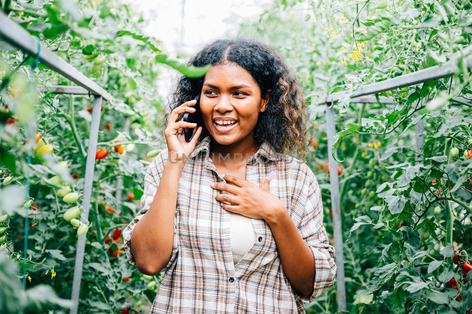 Woman farmer in greenhouse talks on phone by Sorapop