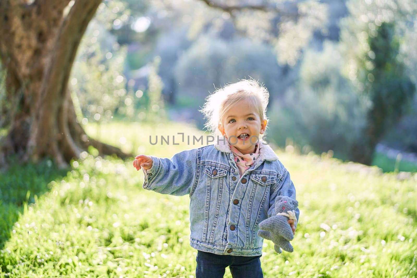 Little smiling girl with a toy walks through the sunny forest by Nadtochiy