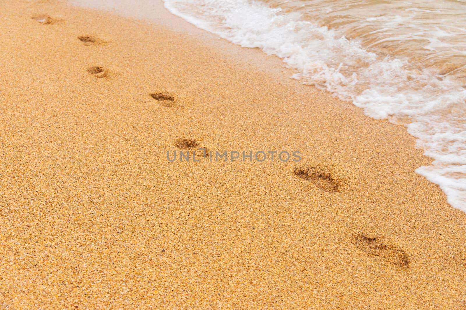 sand, wave and footprints in the daytime. golden sandy beach with sea waves, close-up of solitary human footprints by yanik88