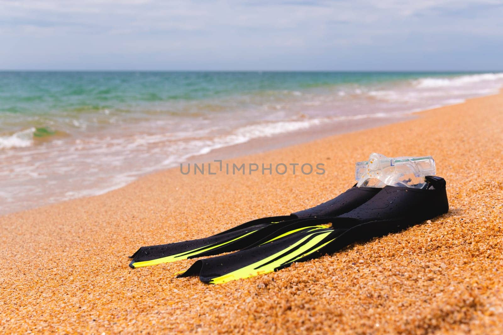 A snorkeling mask with fins lies on a sandy beach overlooking the sea and sky, no people