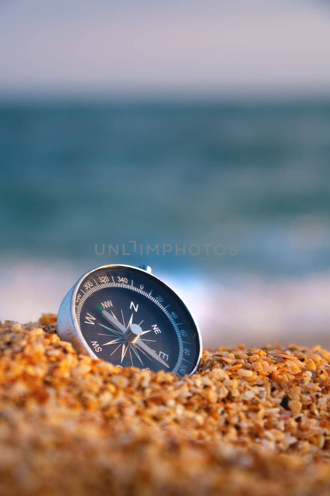 Conceptual photo, close-up of a compass lying in wet sand consisting of small crumbs of shells, against the backdrop of a blue calm sea by yanik88