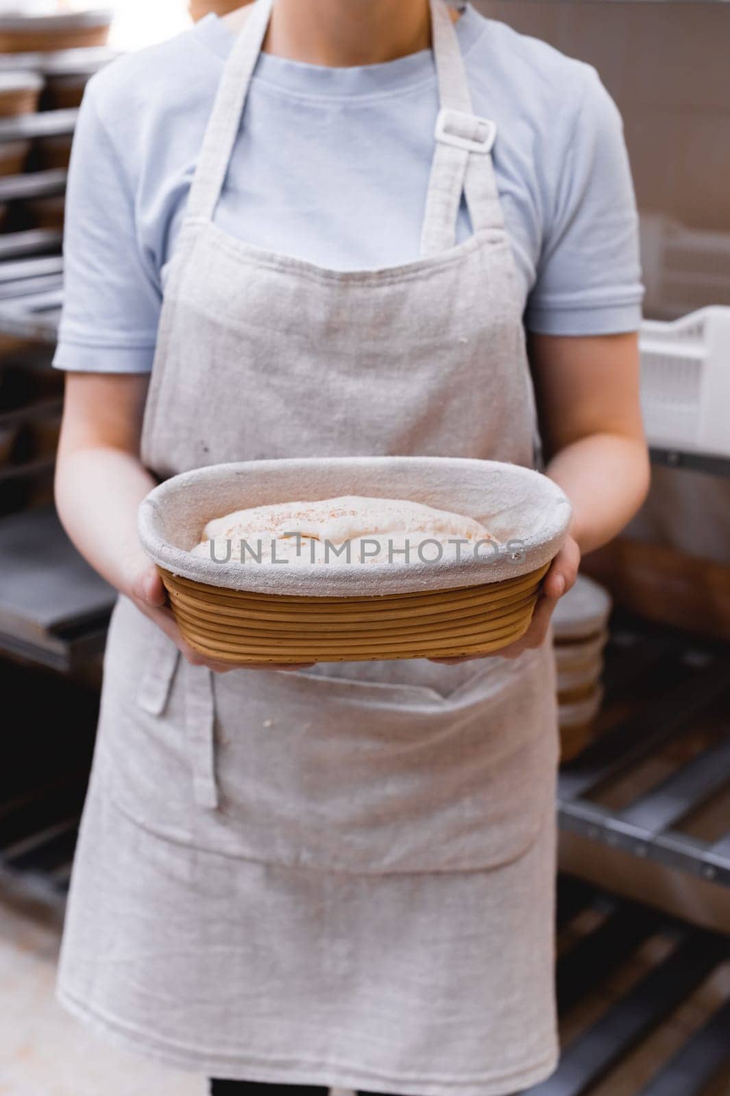 Hands of a baker holding dough in a wooden mold, against the backdrop of a bakery and workplace. prepares ecologically natural baked goods.