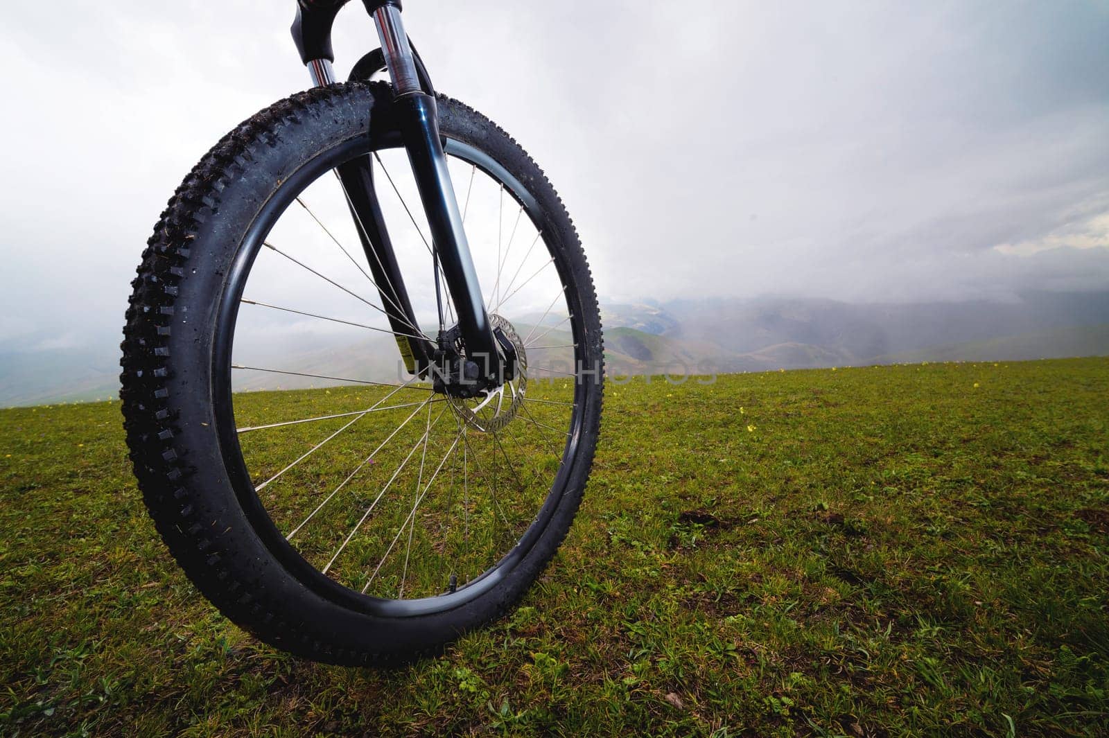 Mountain biker standing on a hill or field, close-up of a wheel. Active and sports recreation concept.
