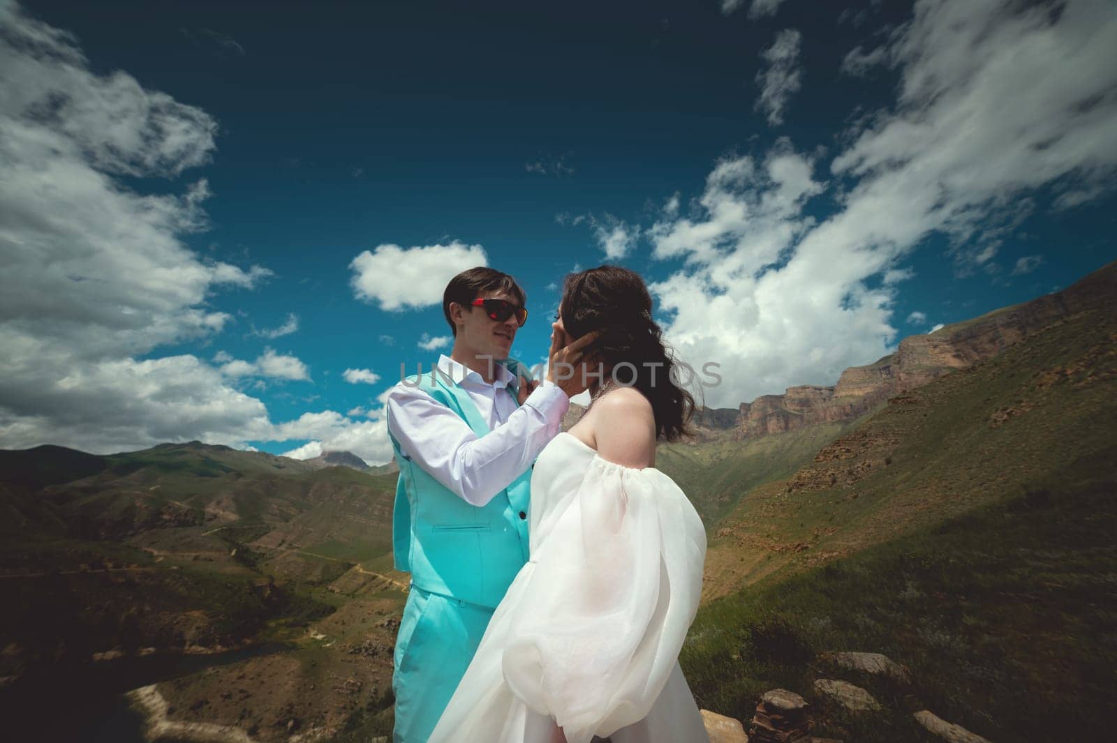 Beautiful wedding couple laughs and plans to kiss against the backdrop of mountains and cloudy sky. Portrait of happy newlyweds.