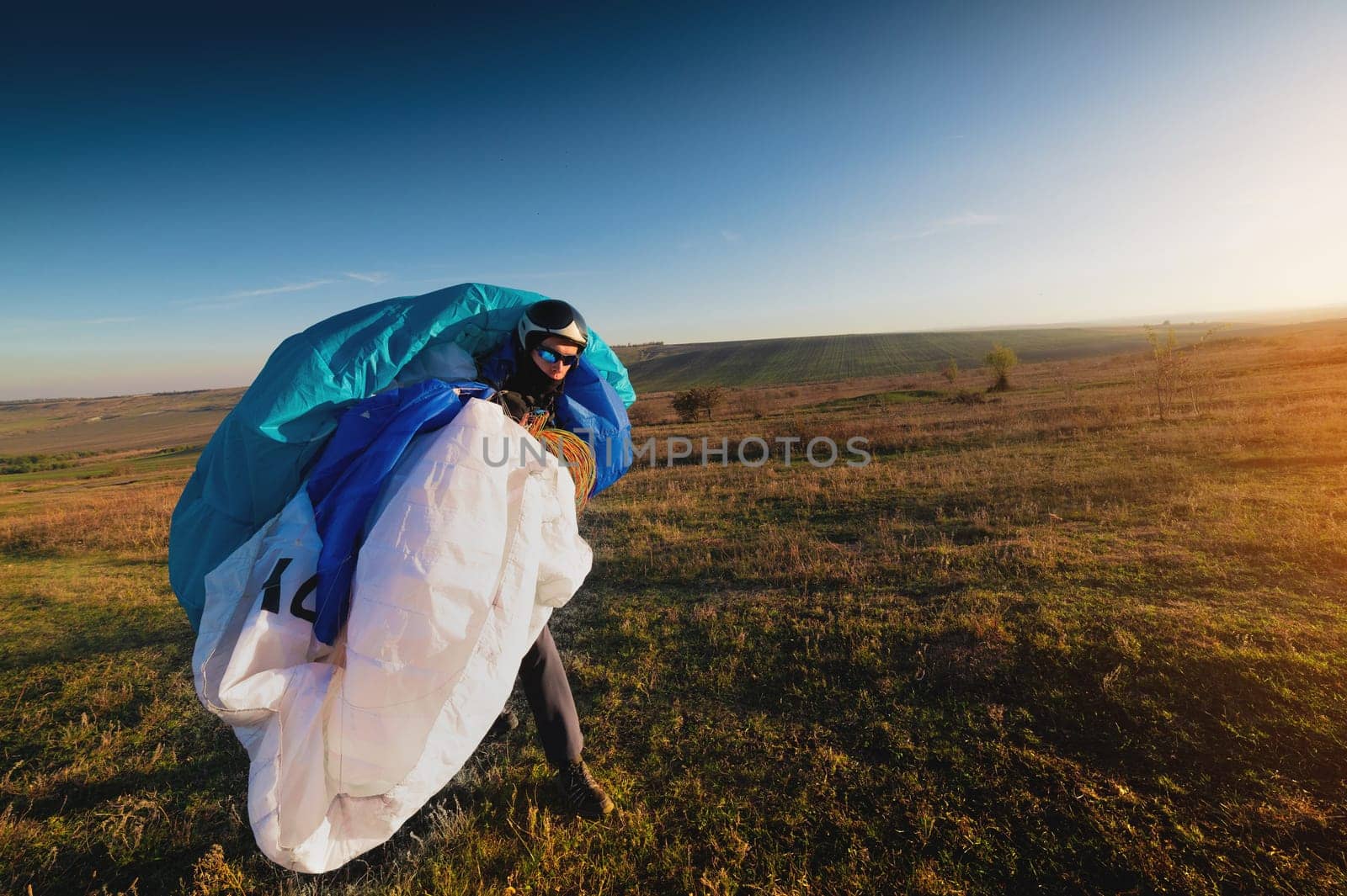 male paraglider with a parachute in his hands on a sunny day on the field. Preparing for a flight or completing a flight, preparing equipment for takeoff by yanik88