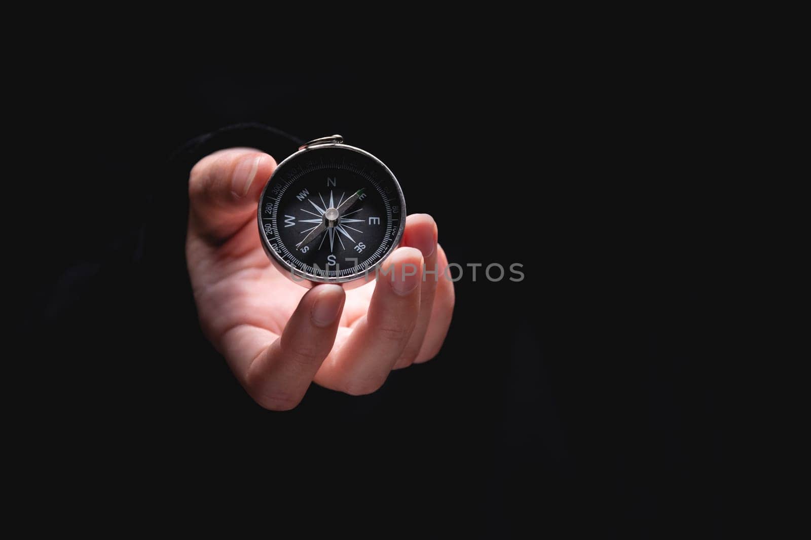 woman hand holds a compass showing south on a black background. A hand from the darkness holds out a compass, the concept of being lost and finding a solution or ideas with meanings by yanik88