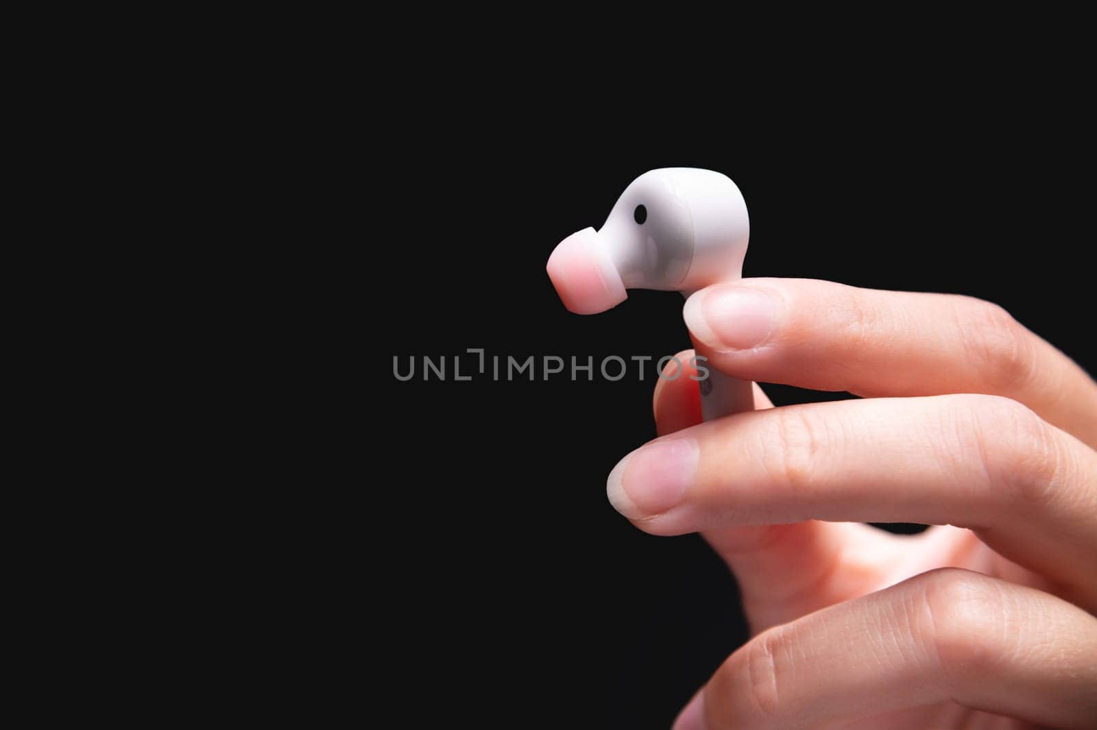White wireless earphone in a woman's hand. Close up of vacuum earphone held in hand on dark background.