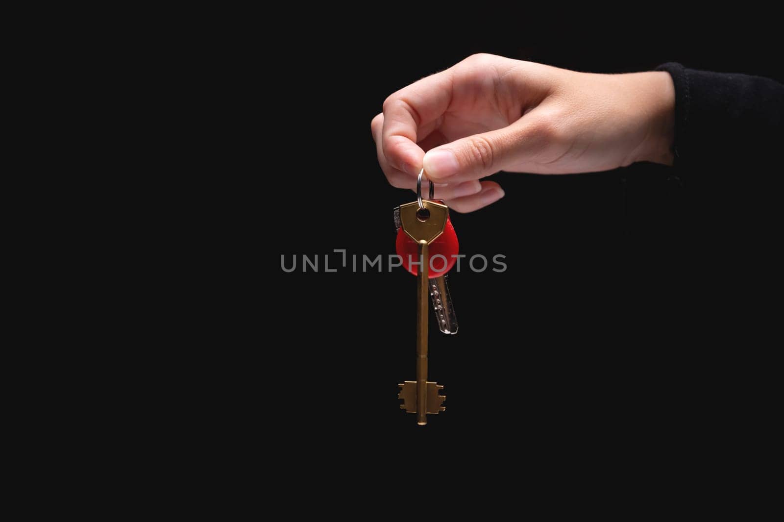 A hand holds the keys to the apartment on a black background. Young adult woman holding metal door keys in her hand, close-up. Blank space for text.