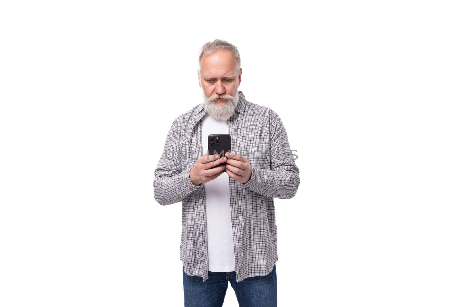 a handsome pensioner man with a beard and a big mustache is dressed in a shirt and jeans chatting on the phone.