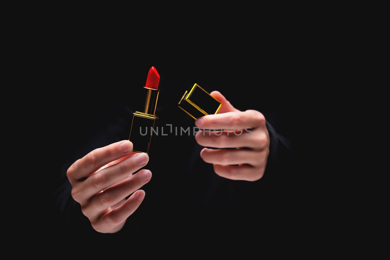 Hand holds red lipstick on black. Female hands opened an elite lipstick in a gold frame, serving a luxury cosmetic product.