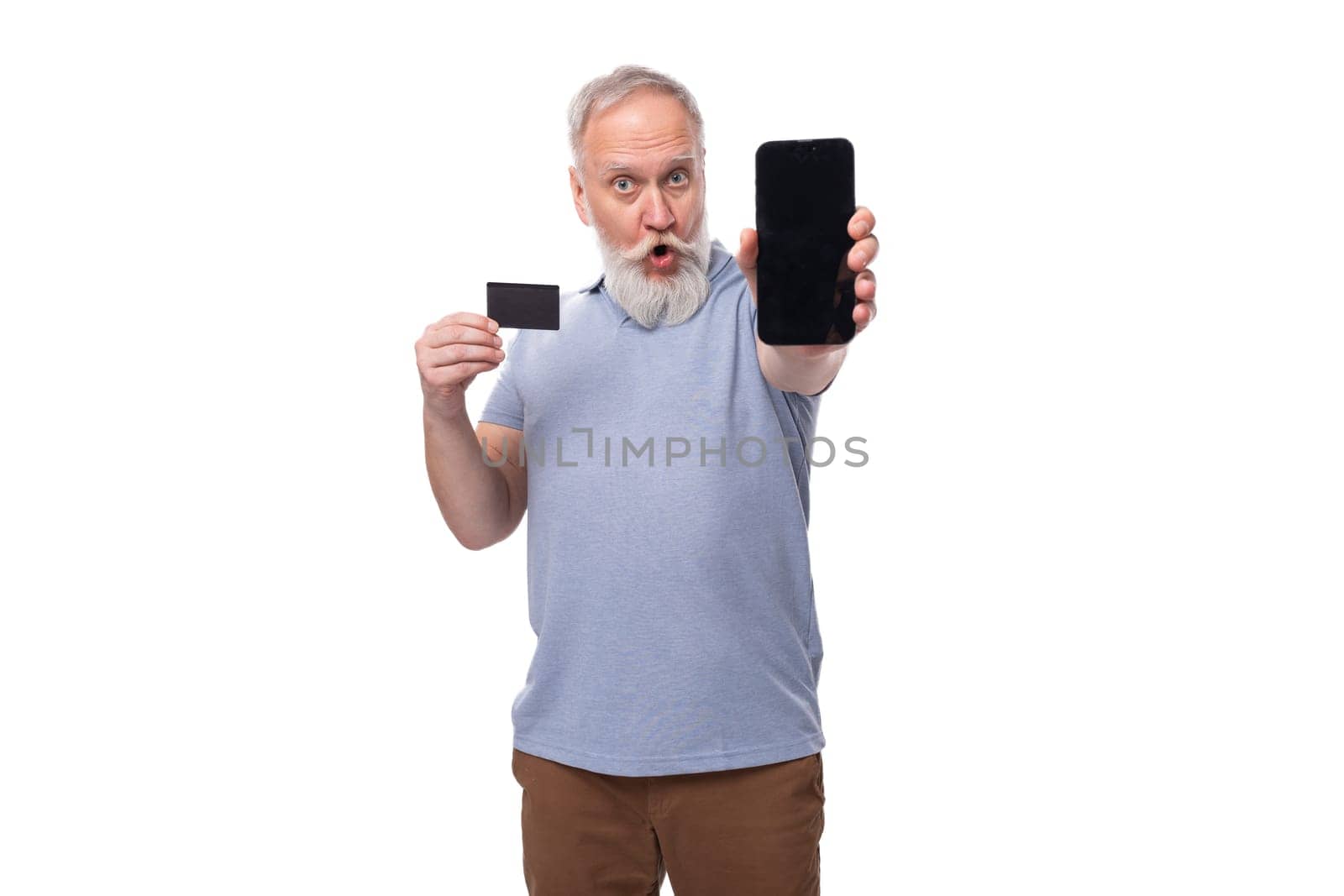 stylish pensioner man with beard and mustache in shirt and trousers holds plastic card mockup and smartphone.