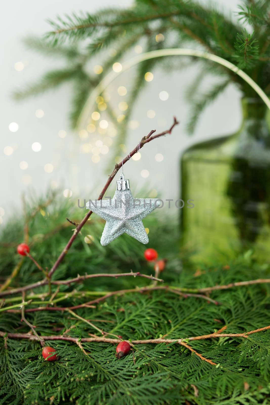 A silver star Christmas ornament hanging on a branch with red berries and greenery in the background. New Year and Christmas concept