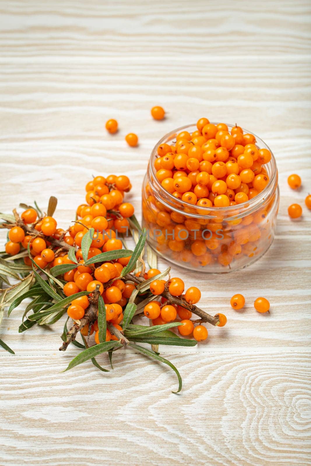 Sea buckthorn ripe berries in glass jar and branches with leaves top view on white wooden rustic background, great for skin, heart, vessels and immune system.