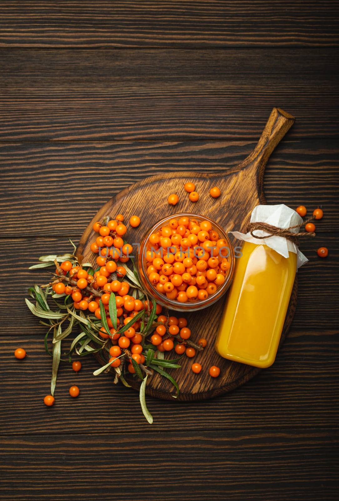 Sea buckthorn healthy drink in bottle, ripe berries in glass jar and branches with leaves top view on dark wooden rustic background, great for skin, heart, vessels and immune system. by its_al_dente