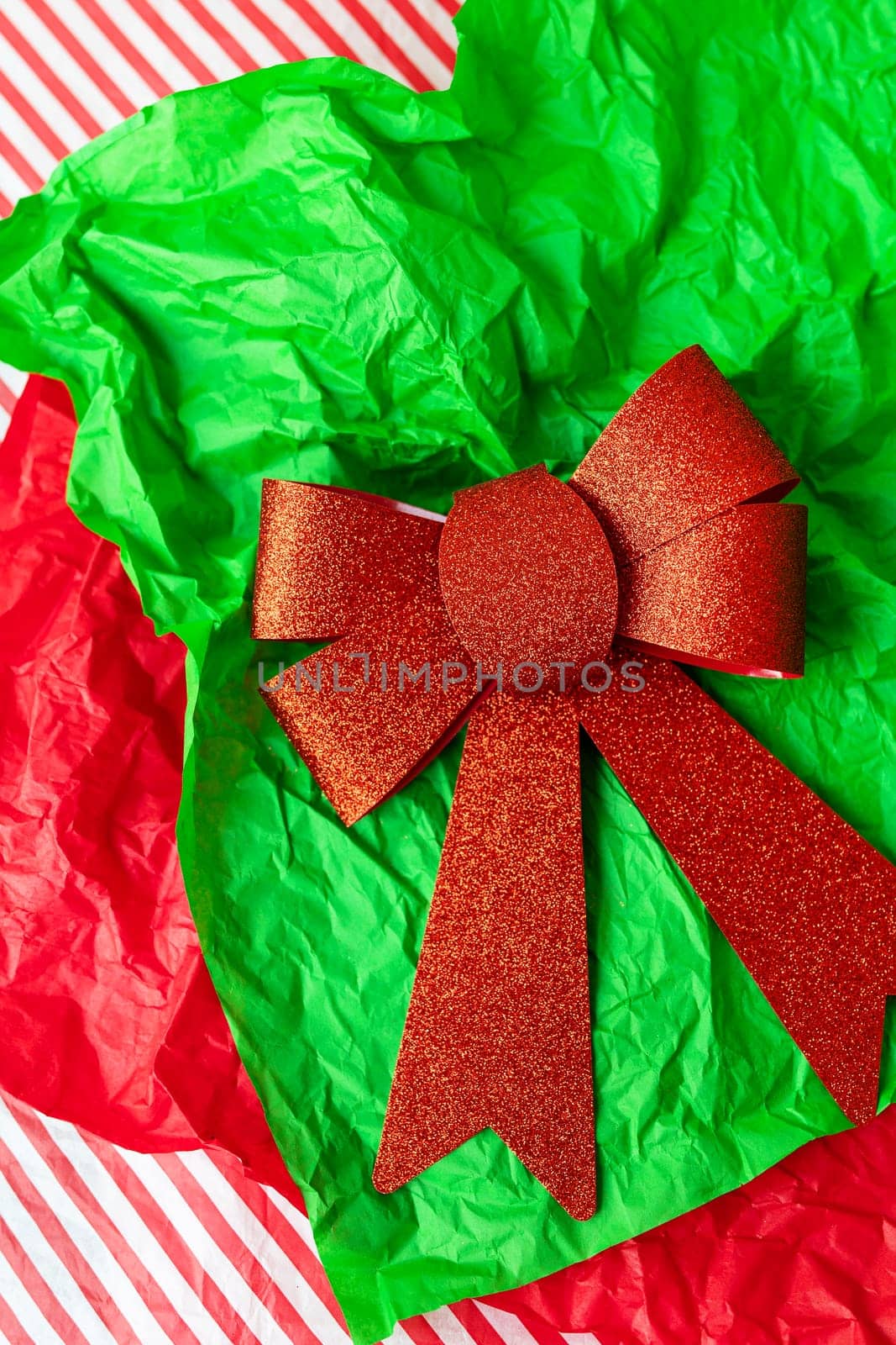 This is a photo of a red glitter bow on a green crumpled tissue paper with a red and white striped background. by sfinks