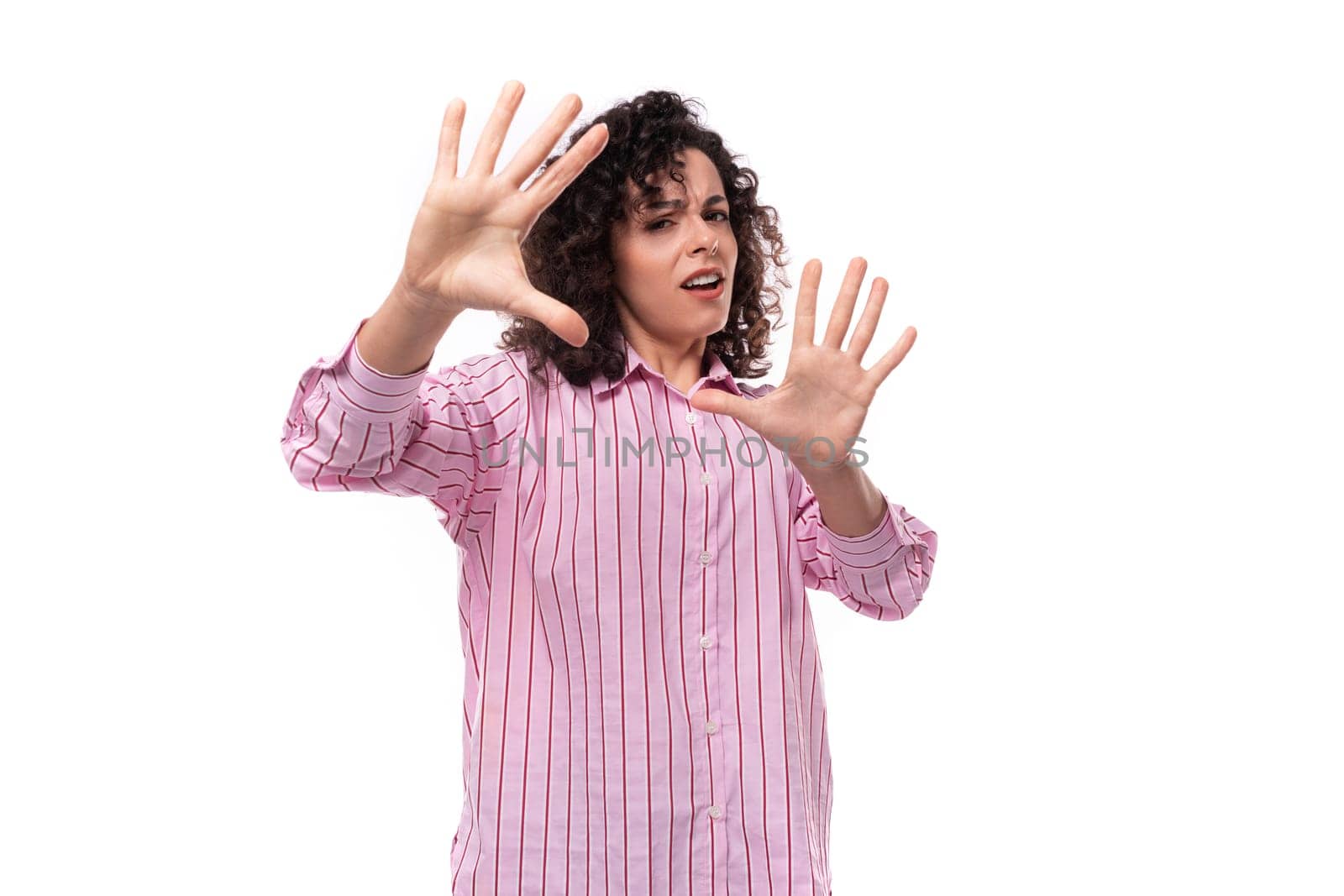young cute curly-haired caucasian woman dressed in a striped pink blouse actively gesticulates with her hands. people lifestyle concept.