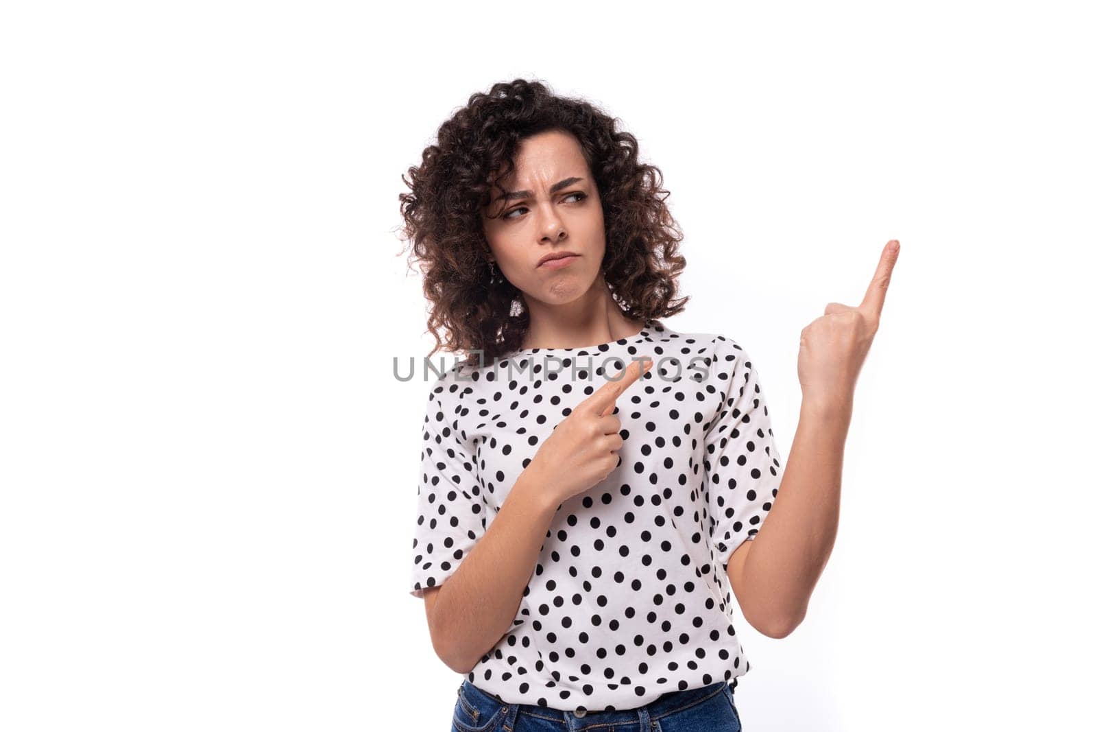young authentic curly brunette slender lady wearing polka dot short sleeve shirt pointing fingers at ad space by TRMK