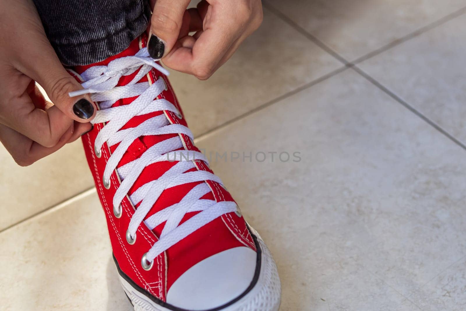 close up of the legs of a beautiful teenage girl. Young hipster woman tying laces in red sneakers by PopOff