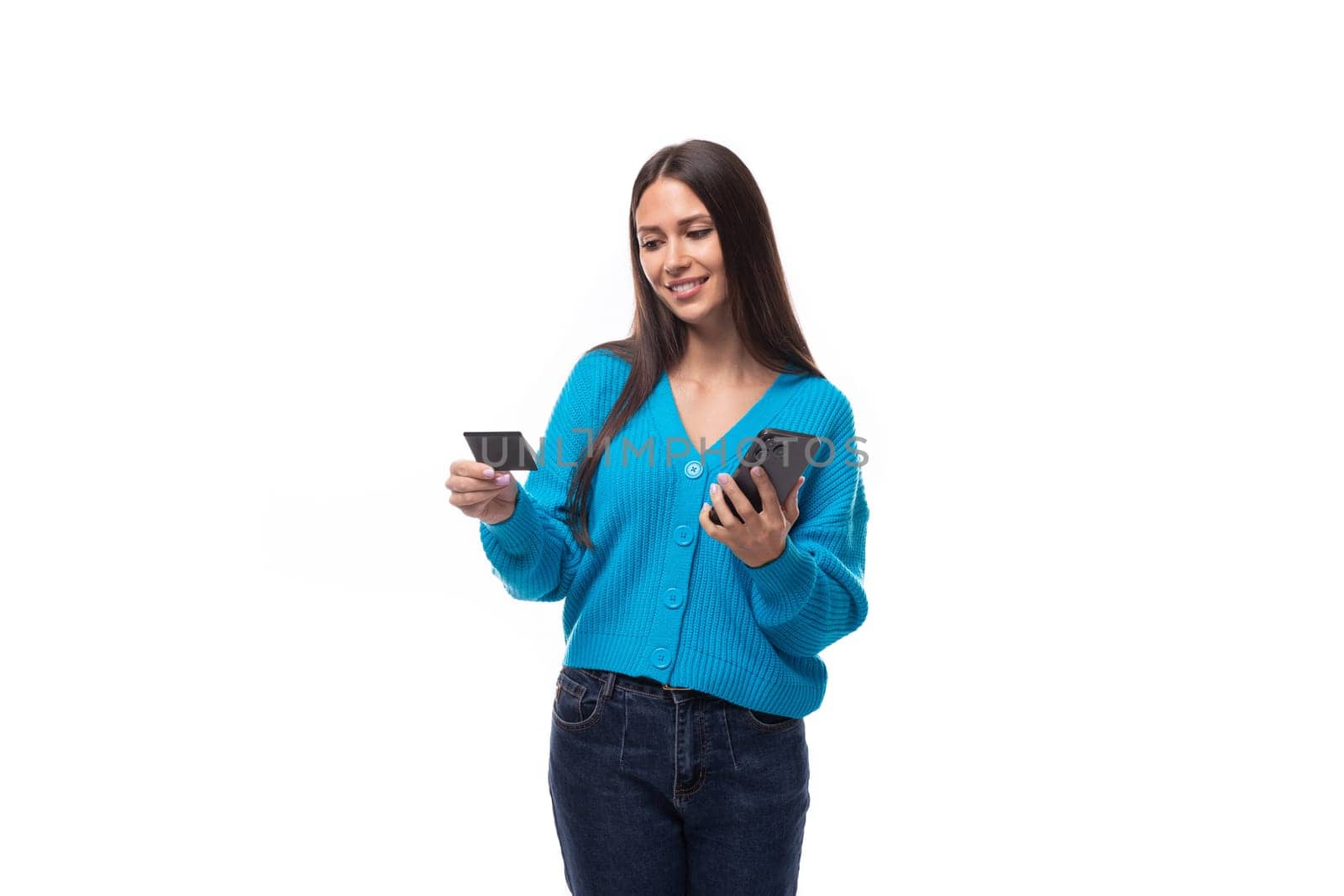 confused young brunette woman dressed in a blue sweater with buttons holds a bank card and a smartphone. e-business concept by TRMK