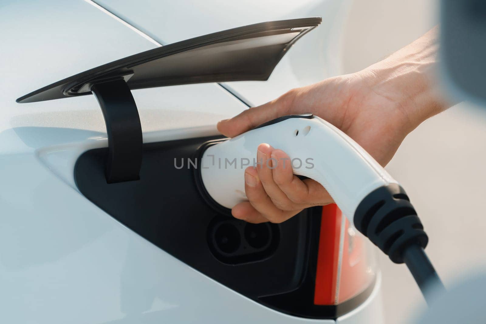 Closeup hand put EV charger to recharge electric car's battery from charging station in city commercial parking lot. Rechargeable EV car for sustainable environmental friendly urban travel. Expedient