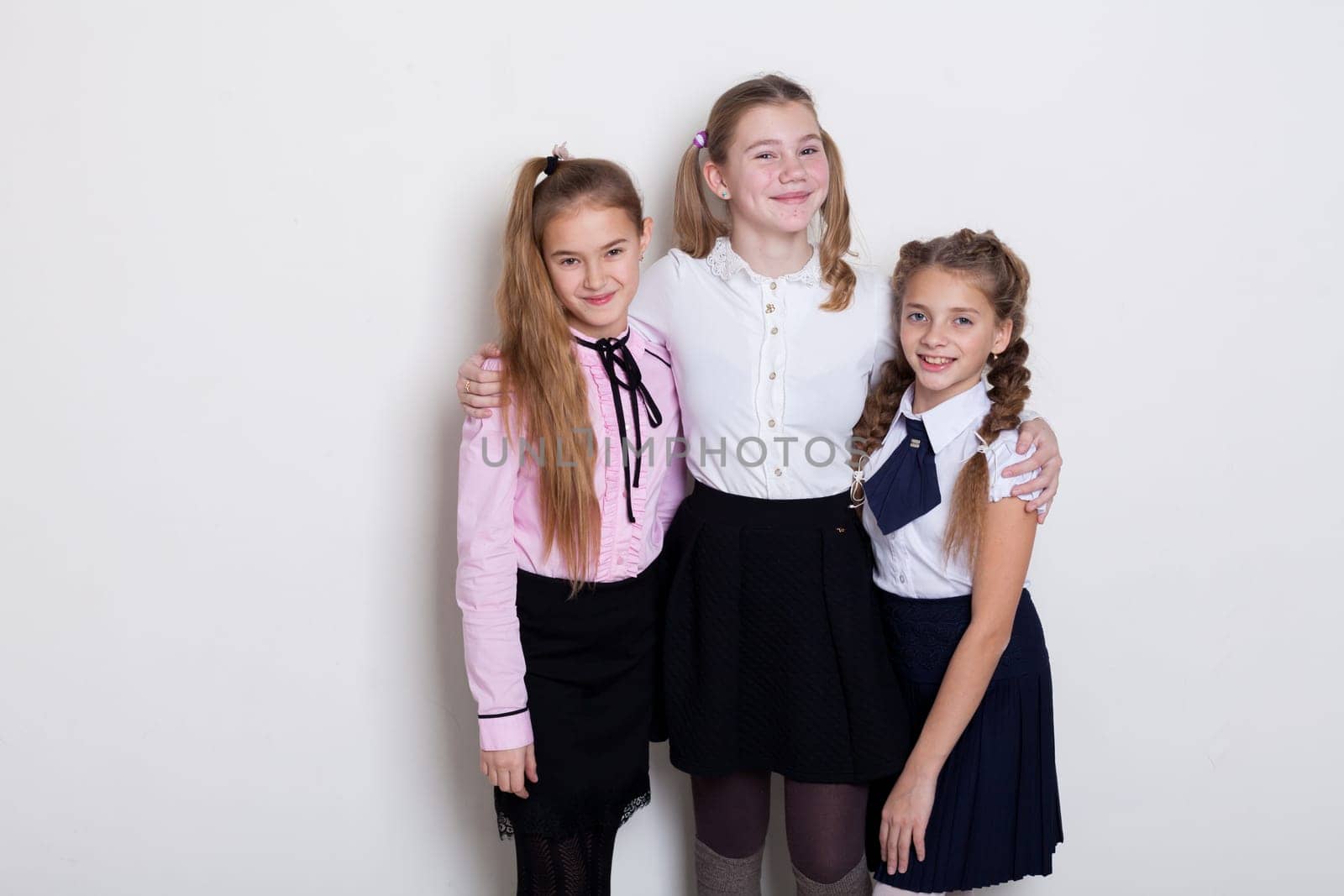 three schoolgirl girls in class at the white wall