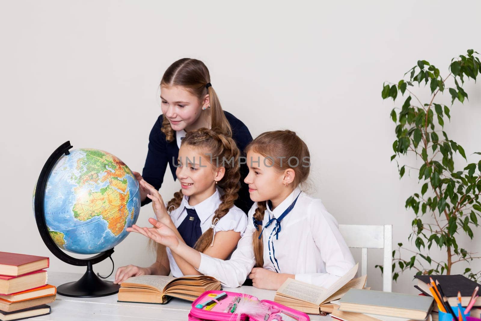 three schoolgirl girls with books and a globe in geography class at the desk