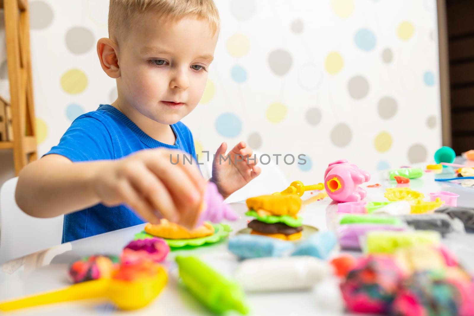 Little boy enthusiastically plays with plasticine, play dough on white table by andreyz