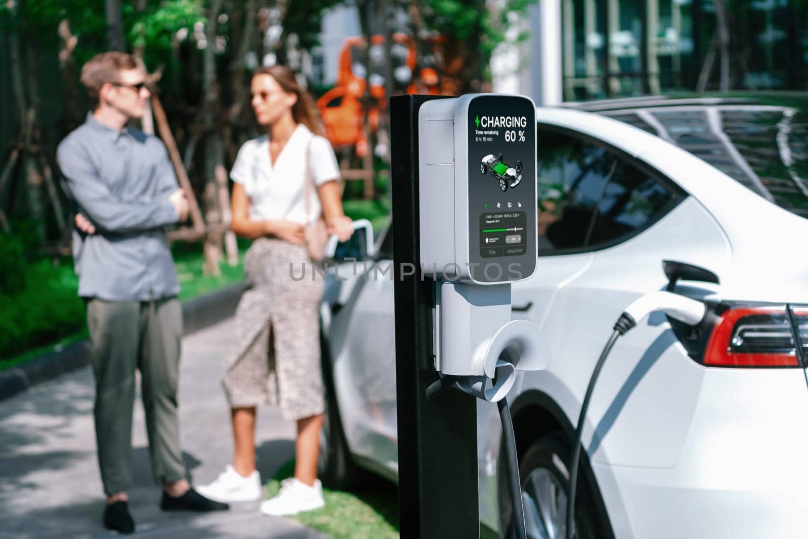 Young couple travel with EV electric car charging in green sustainable city outdoor garden in summer shows urban sustainability lifestyle by green clean rechargeable energy of electric vehicle innards