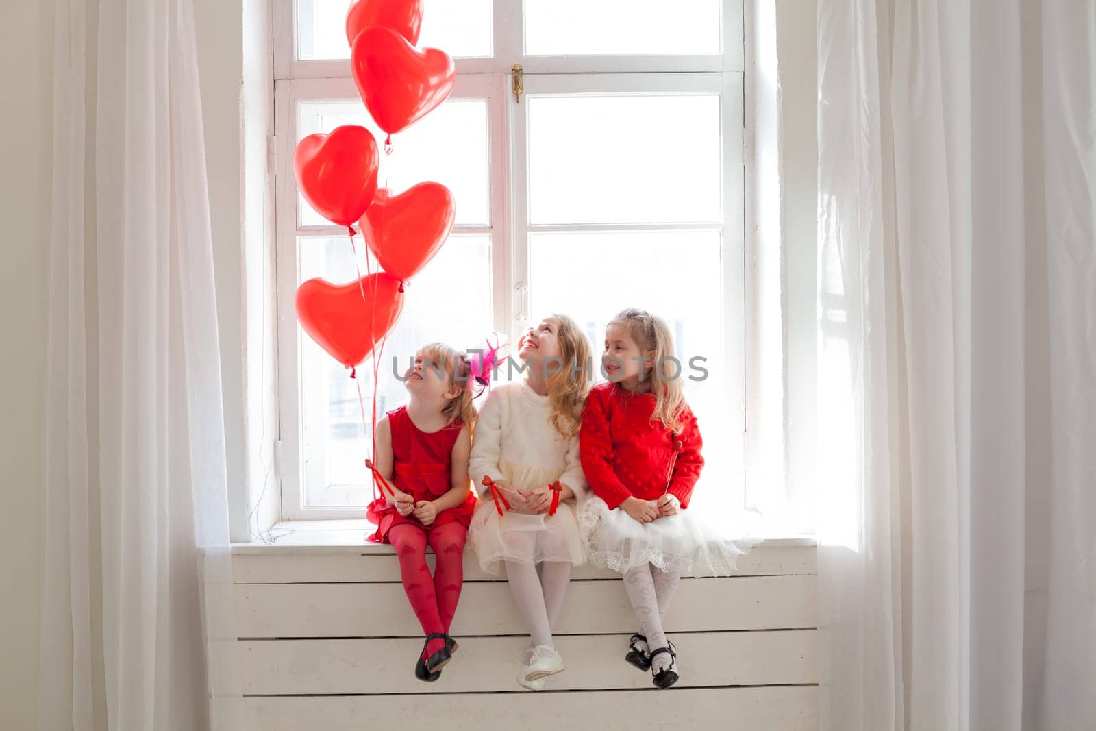 Three beautiful little girls with balloons in red and white dresses at the party