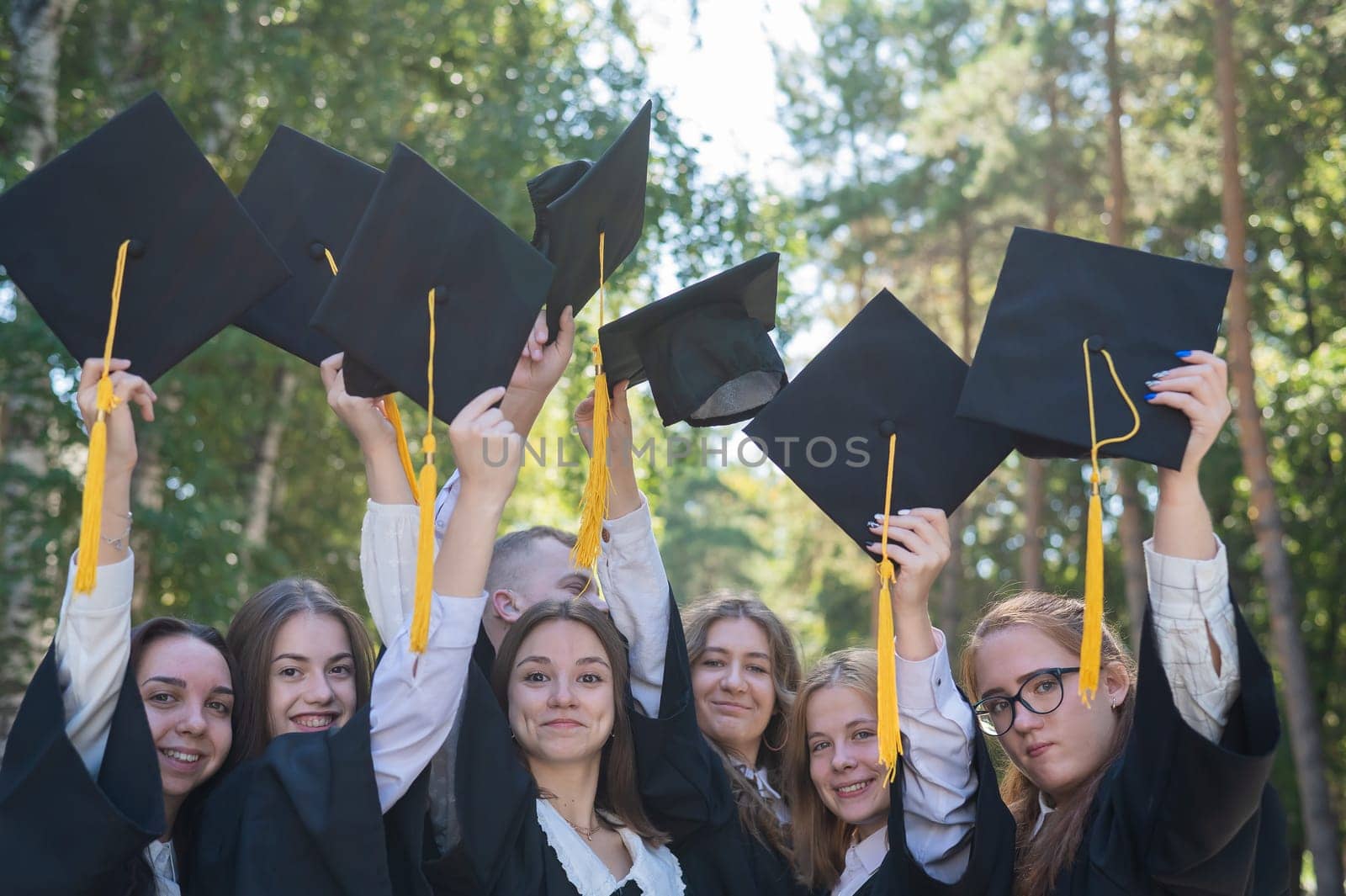 Classmates in graduation gowns throwing hats outdoors