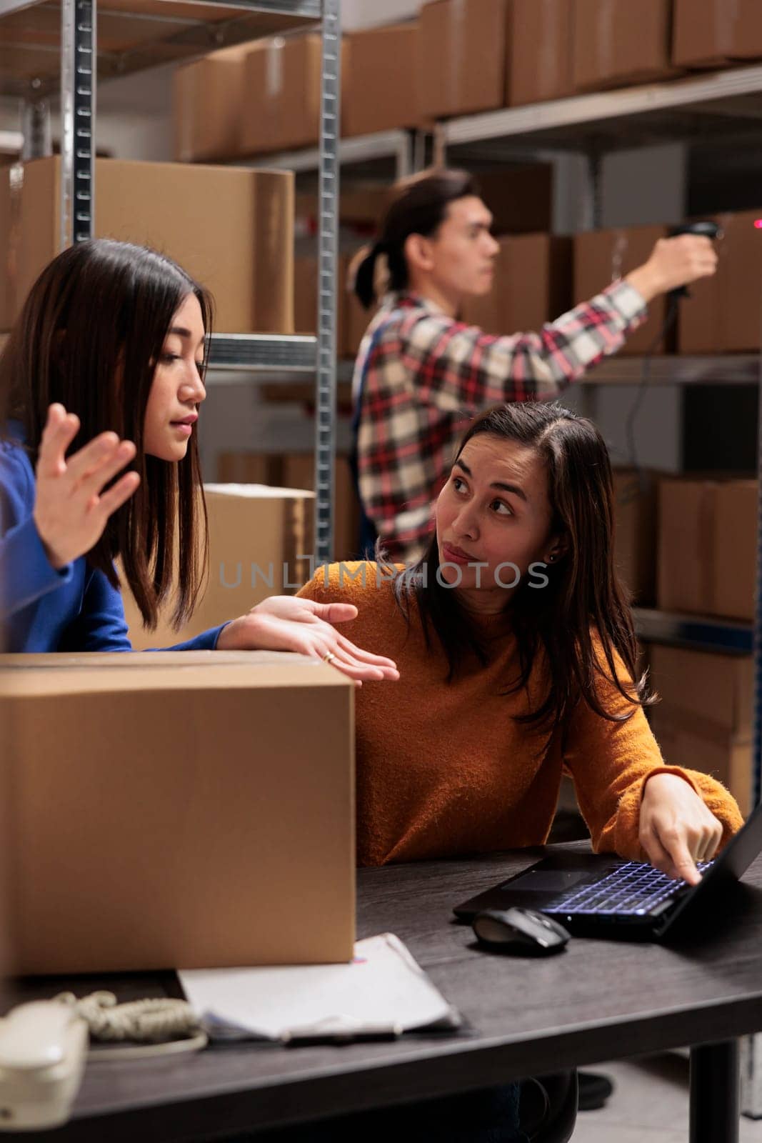 Warehouse operator supervising coworker doing inventory on laptop in storage room. Storehouse young asian women employees discussing goods logistics and distribution schedule