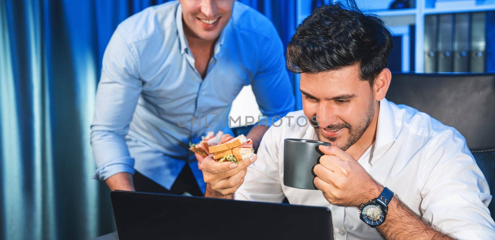 Business partners with happy smiling face sharing delicious sandwich dish with friend at night time. Hungry creative colleagues enjoy eating fast food at workplace with neon blue light. Sellable.