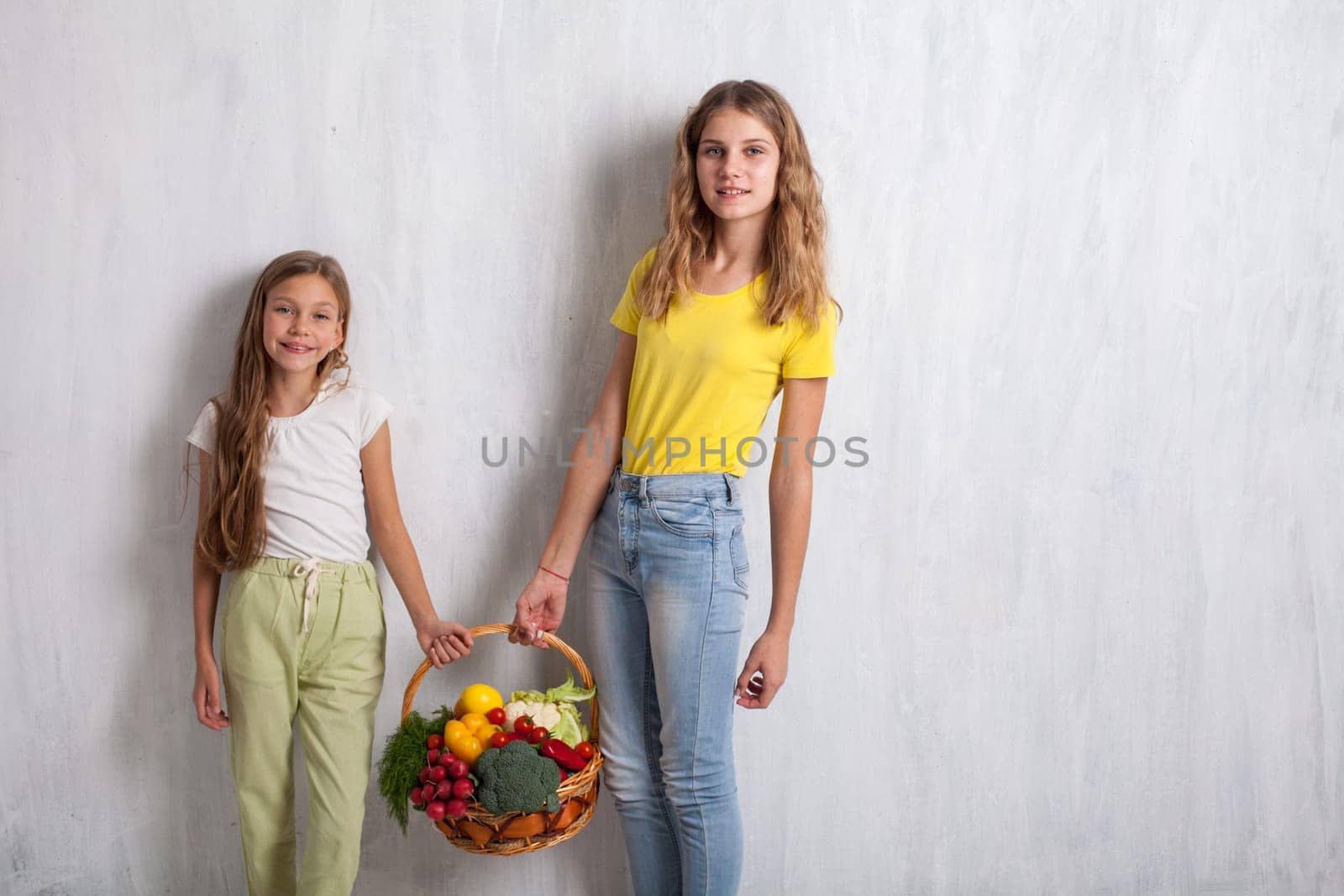 Two girls holding a basket of ripe vegetables