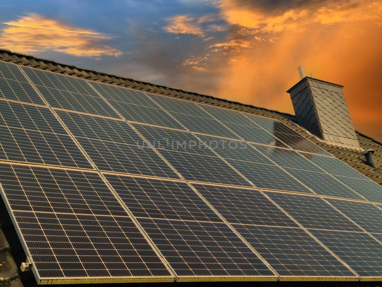 Lots of solar panels producing clean energy on a roof of a residential house during sunset