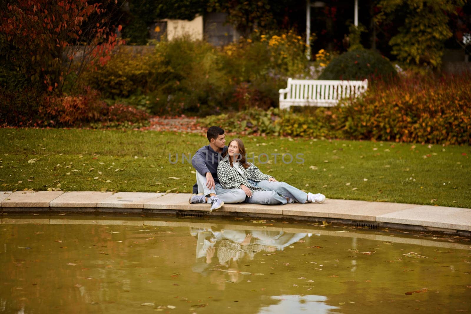 Young couple kissing and rejoices at the lake. lovely young couple kissing outdoors in autumn. Loving couple walking in nature. Autumn mood. Happy man and woman hugging and kissing in autumn. Love. Fashionable couple outdoors. Fashion, people and lifestyle. Stylish couple in autumn outfit. by Andrii_Ko