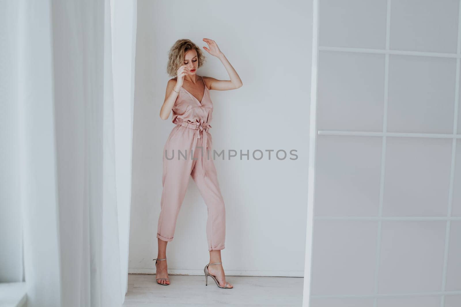 Portrait of a beautiful fashionable blonde woman in a pink jumpsuit in a white room