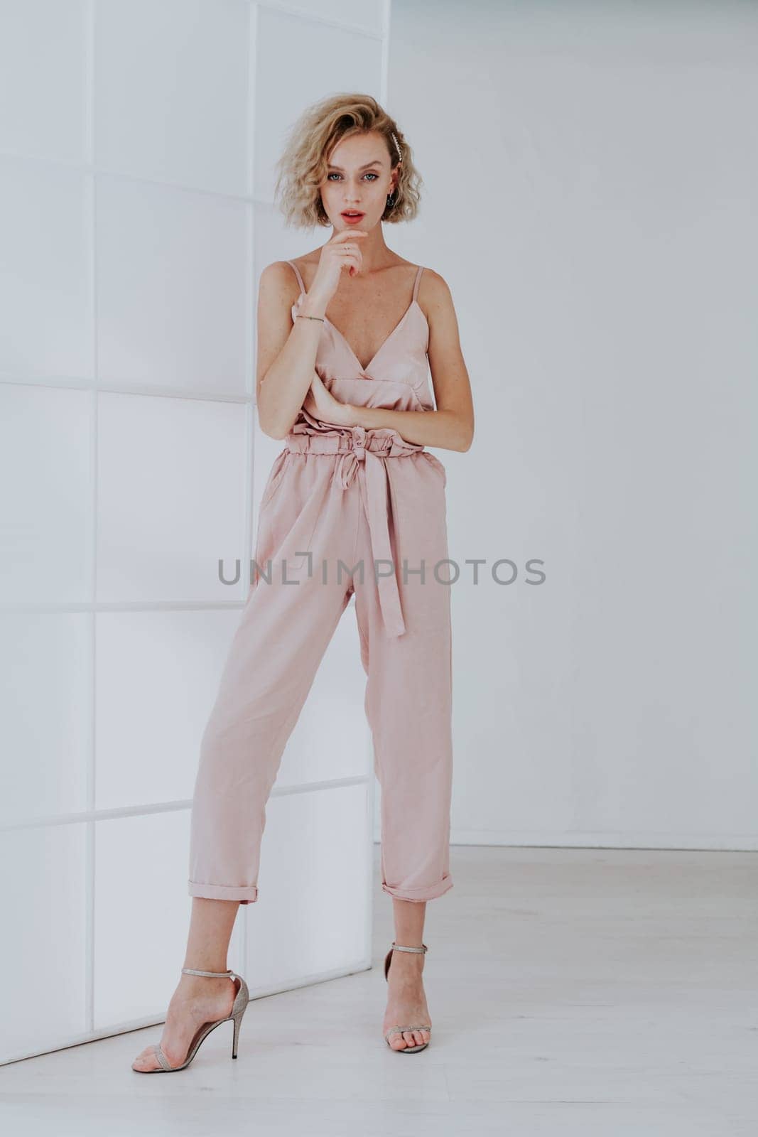 Portrait of a beautiful fashionable blonde woman in a pink jumpsuit in a white room