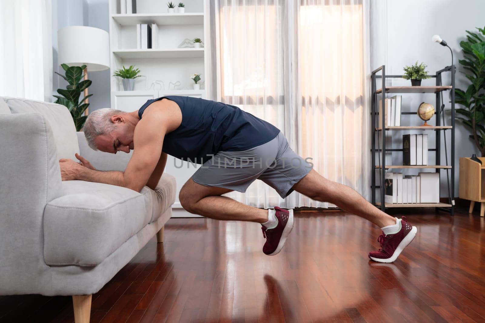 Active and fit senior man warmup and stretching using furniture before home exercising routine at living room. Healthy fitness lifestyle concept after retirement for pensioner. Clout