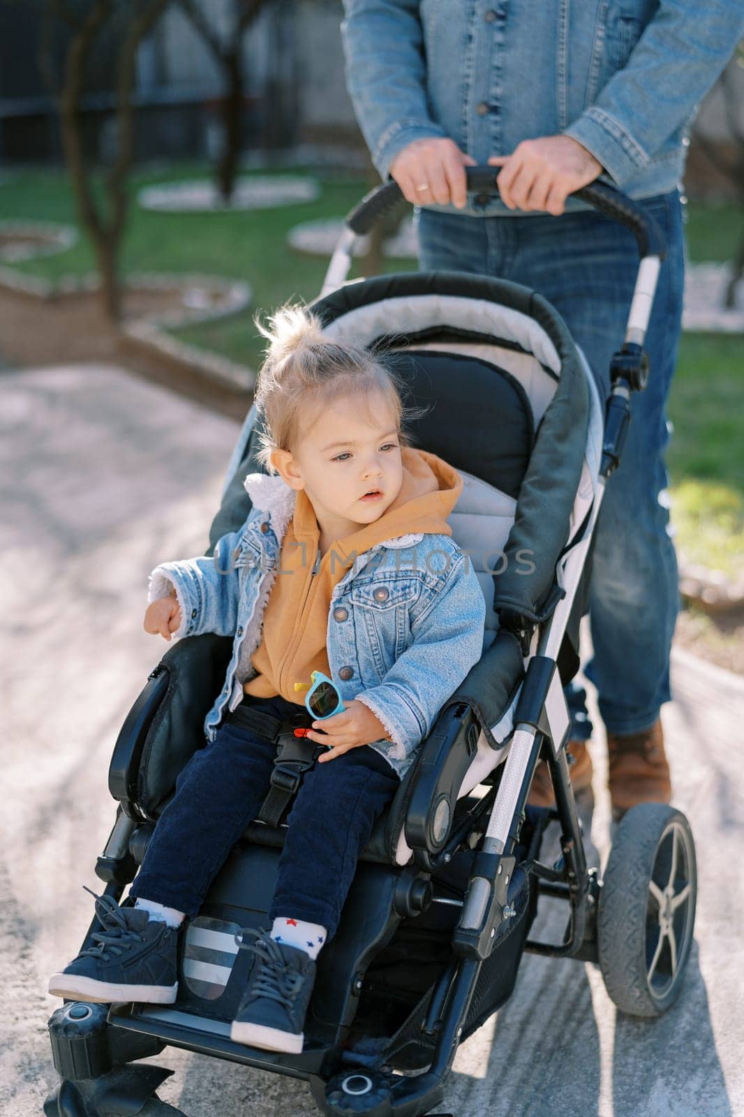 Dad is holding a stroller by the handle with a little girl sitting in it. Cropped. High quality photo