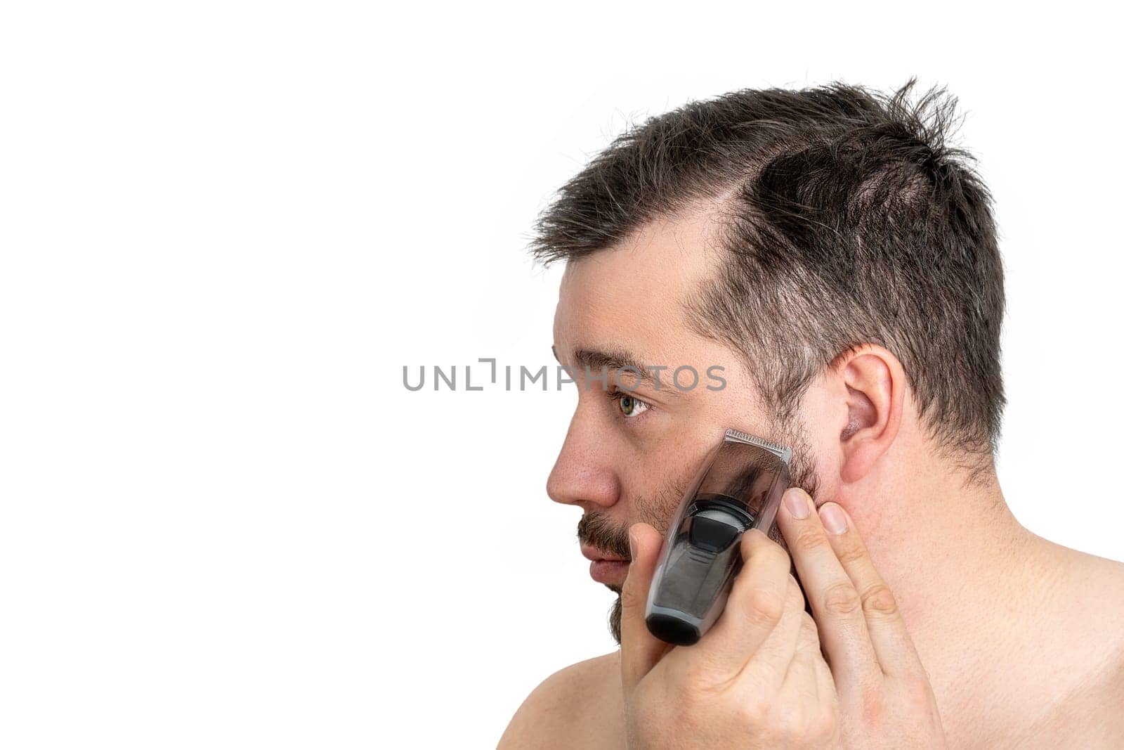 Close-up of a young man shaving his face with an electric razor, isolated on a white background. The man is focused and engaged in his grooming routine.