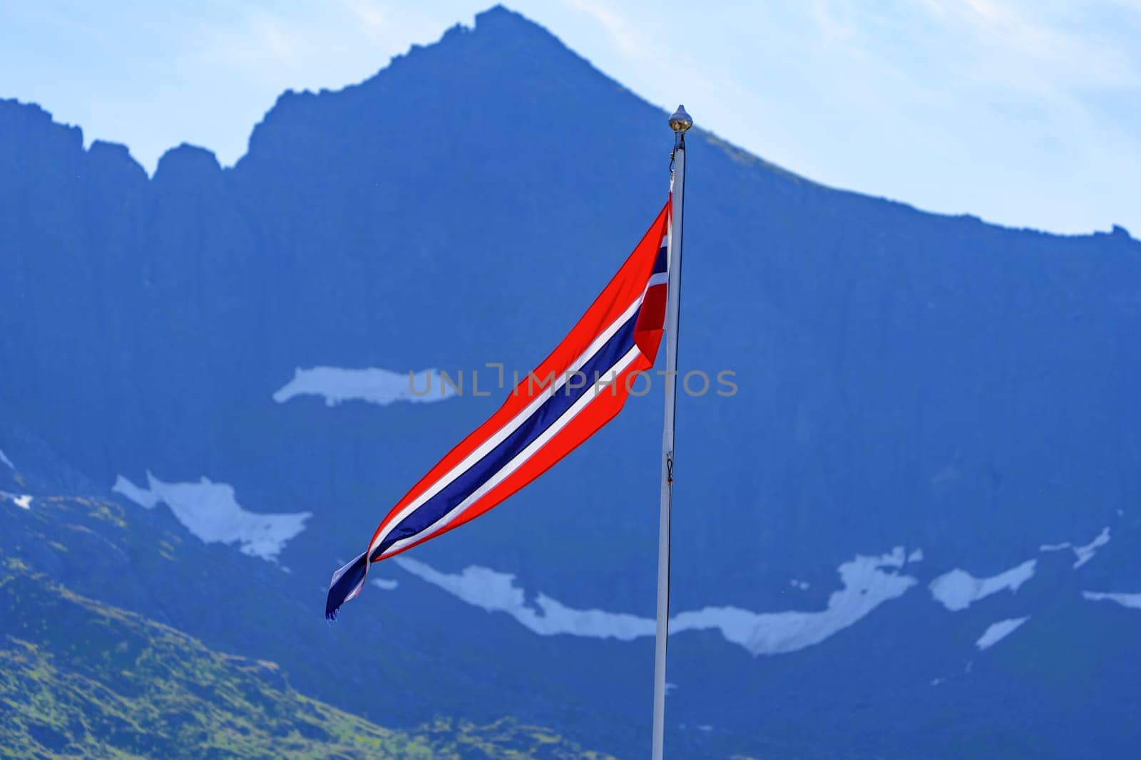 A breathtaking scenic view of the Norwegian flag proudly waving against a backdrop of a majestic mountain range. The vibrant colors and stunning landscape capture the natural beauty of Norway.