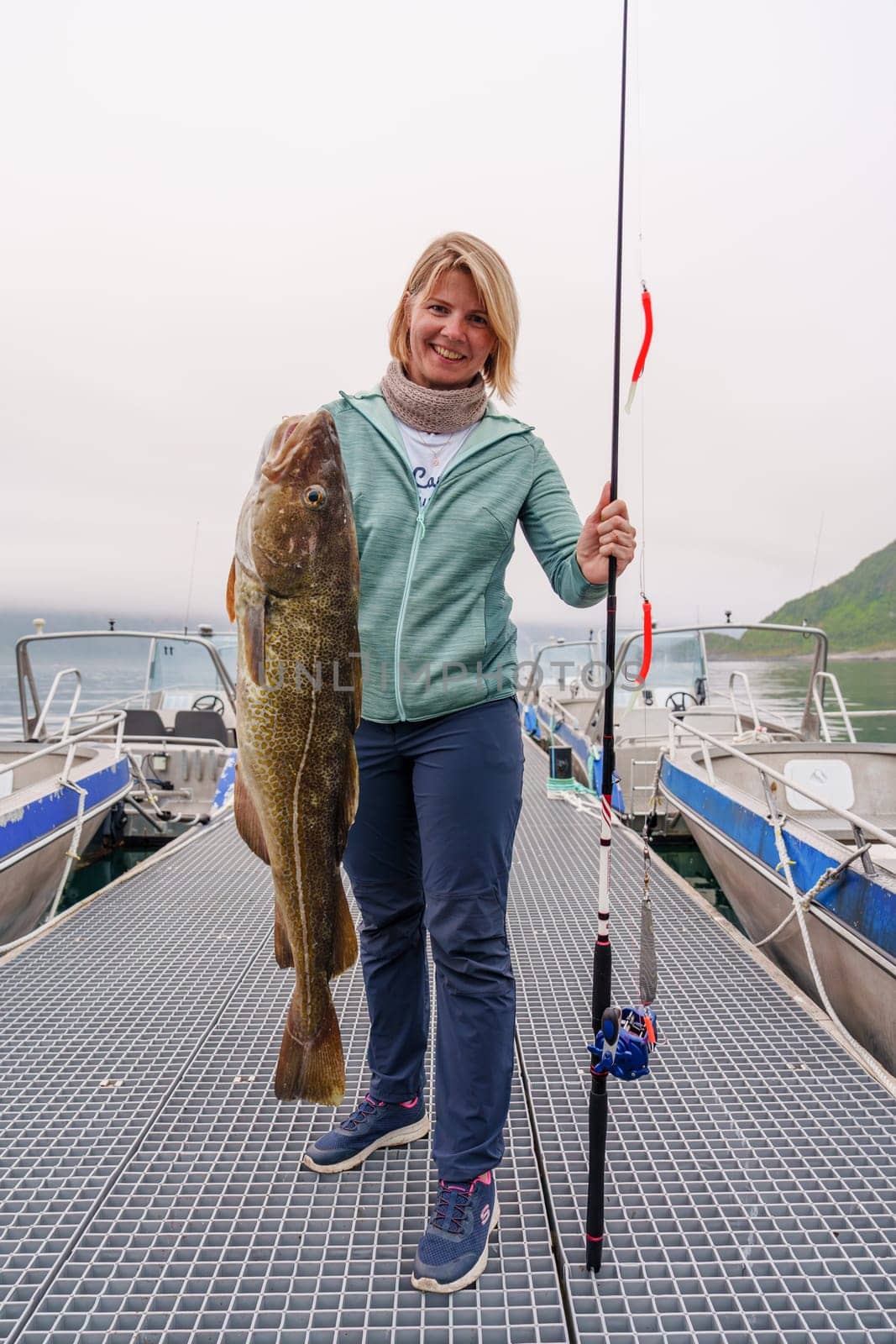 Happy Fisherwoman holding big arctic cod. Norway happy fishing. Woman with cod fish in hands by PhotoTime