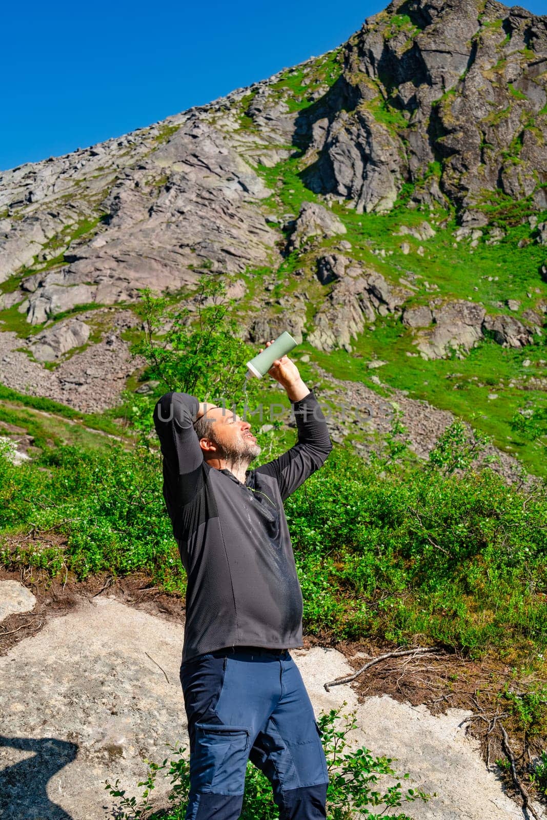 Amidst the breathtaking mountain wilderness, a traveler rejuvenates by enjoying cold water to cool down on a hot sunny day. The serene environment adds to the refreshing experience.