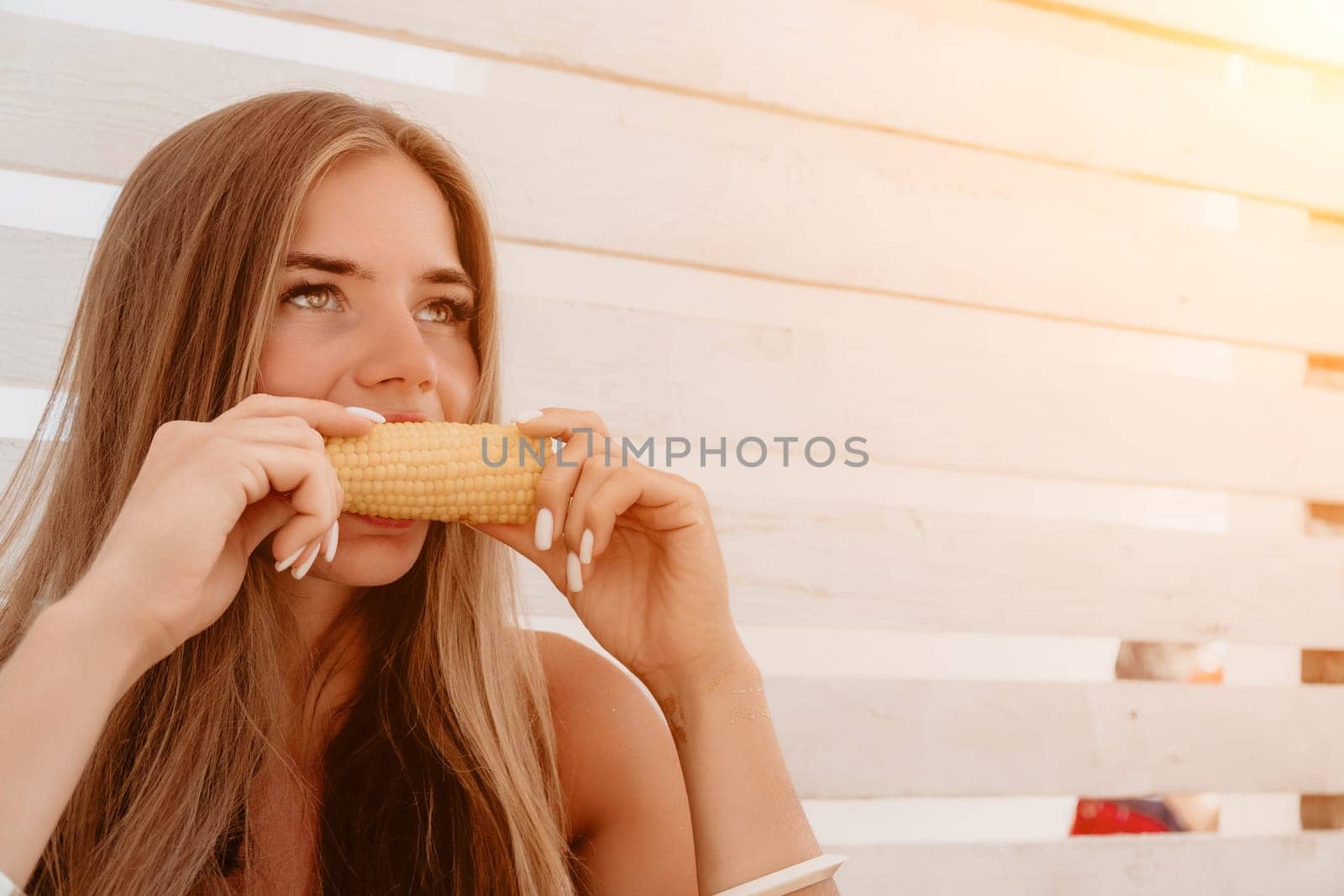 Healthy vegetarian hipster woman in summer outfit eat grilled corn and look to camera. Sexy lady on sea beach sunset or ocean sunrise. Travel, explore, active yoga and meditation lifestyle concept.