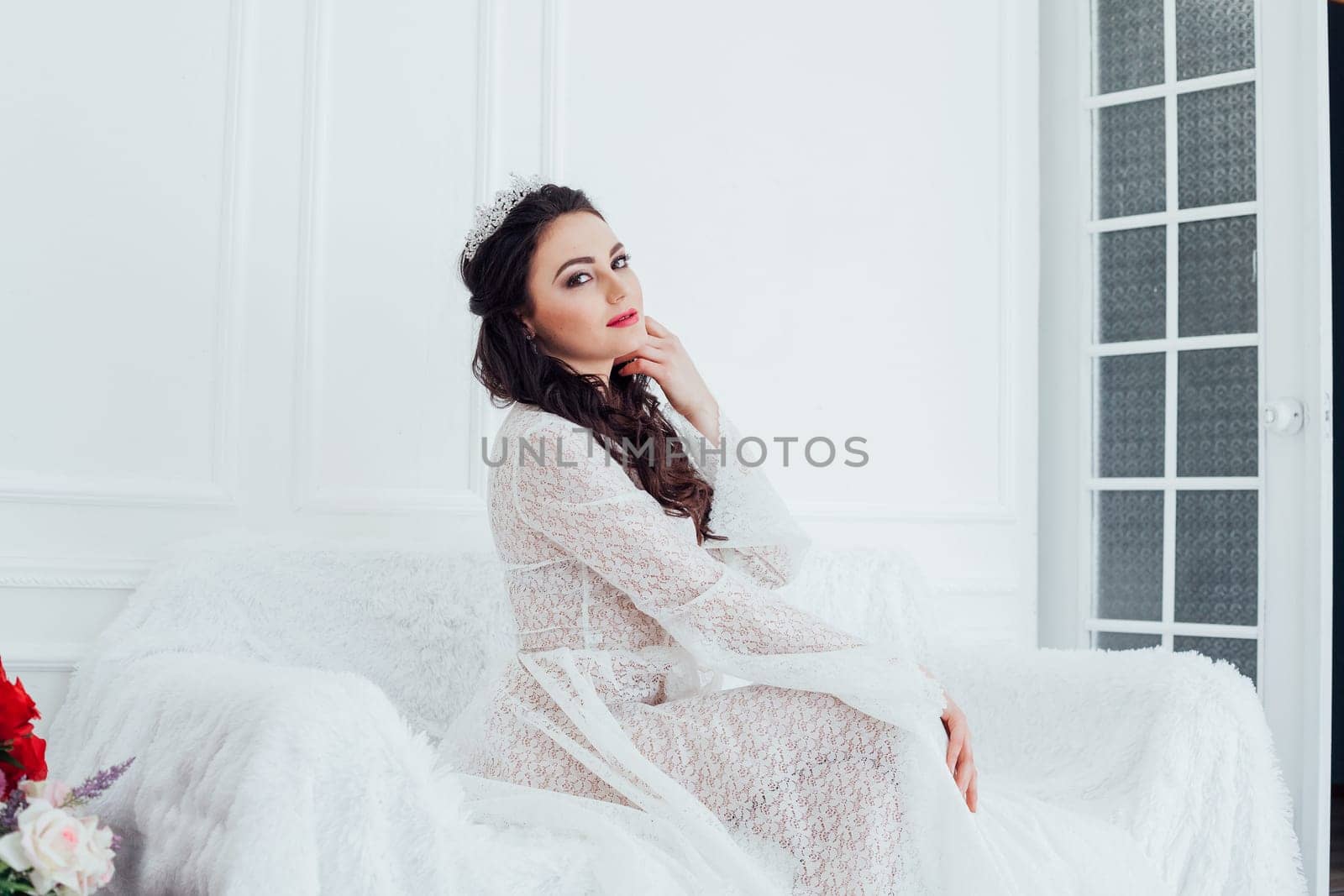 the bride in a wedding dress with a Crown sitting on a white sofa in a room